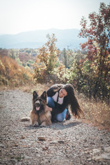 Happy girl with her german Shepherd dog sitting on the dirt road in the forest