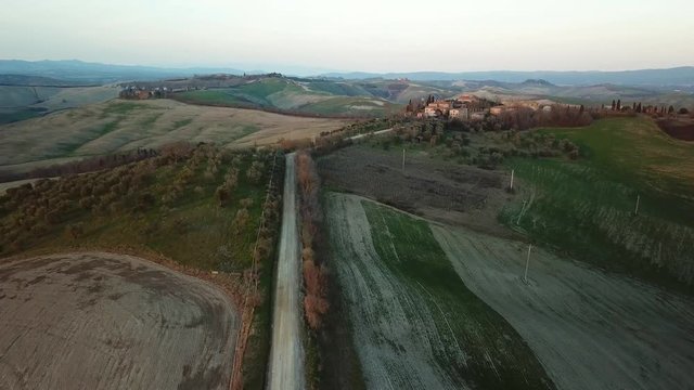 Aerial approach along a country road to a Tuscany old stone village at sunset over a hiils