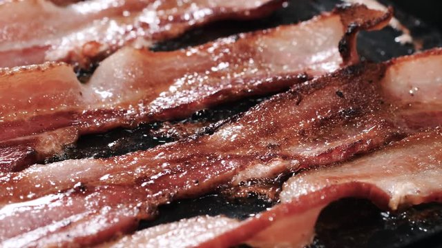 Transfering Curled Up Bacon From The Stove To The Plate. Closeup, panning shot of a hand placing oily, crispy, curled up bacon pieces from frying pan to white plate.