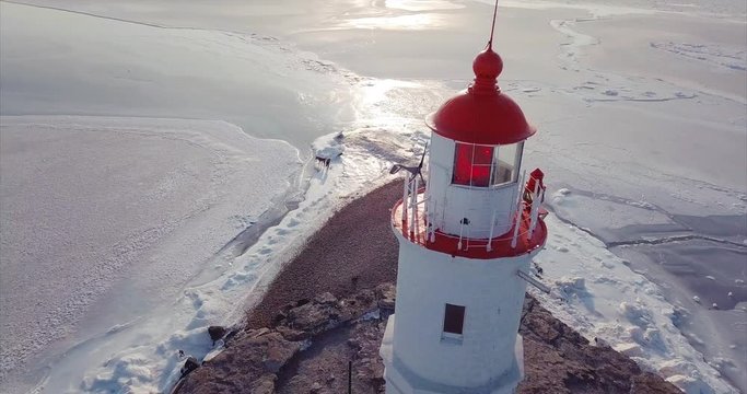 Top aerial panoramic view of a lighthouse perched on a Tokarevsky Spit and Russian bridge across frozen Eastern Bosphorus strait. Vladivostok, winter morning