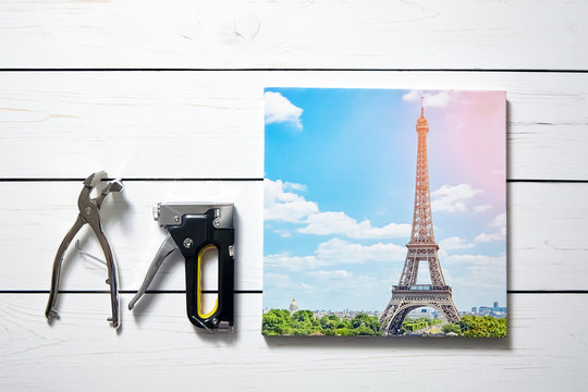 Canvas print. Photo with gallery wrap method of canvas stretching on stretcher bar. Canvas pliers, stapler and photography with image of The Eiffel Tower (Paris, France) on wooden table