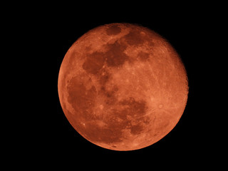 Extreme zoom photo of redish full moon as seen in deep darkness