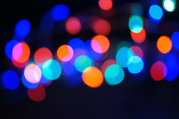Multi-color blue holiday garland. Garland is blurred. Many big colorful round lights. Fully defocused photo. Blurred background and foreground. Holiday mood. New Year and Christmas is coming.