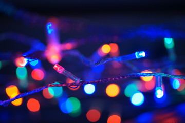 Fototapeta na wymiar Multi-color blue holiday garland. Garland is blurred. Many big colorful round lights. Fully defocused photo. Blurred background and foreground. Holiday mood. New Year and Christmas is coming.