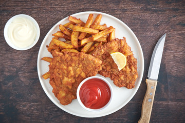 Original Schnitzel mit Pommes und Messer auf Holztisch top view closeup 