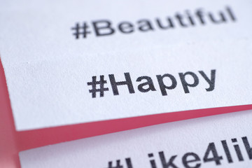 Obraz premium Popular hashtag 'happy' printed on white paper on a pink background. Close up.