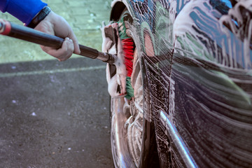 Fototapeta na wymiar Car wash with a brush. The washer washes the wheels of a black car with a brush in the active foam