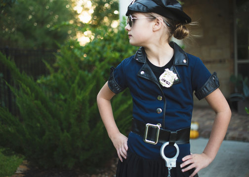 Confident girl wearing police costume with hands on hip standing against plants in yard during Halloween