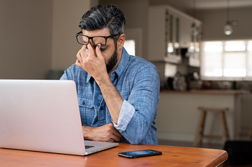 Stressed businessman with laptop computer on wooden table sitting at home