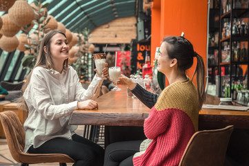 Two happy women are sitting in a cafe, drinking milkshakes,