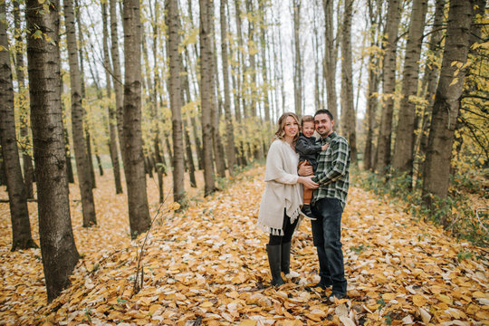 Portrait of smiling family standing against tree trunks in forest during autumn