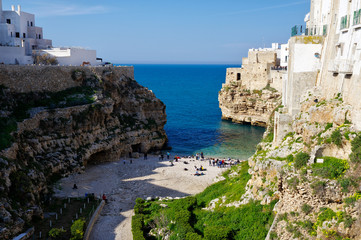 Fototapeta na wymiar POLIGNANO A MARE, ITALY - MARCH 29th, 2018: People on lovely beach Lama Monachile with dramatic view of cliffs with caves rising from Adriatic sea in Polignano a Mare, Puglia, Italy
