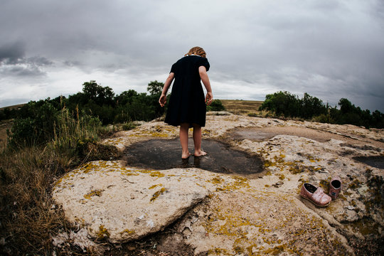 Rear view of girl standing in water on rock against cloudy sky