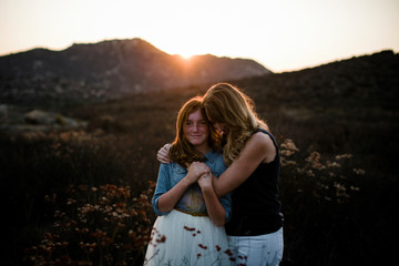 Mother embracing daughter while standing on field against mountains during sunset