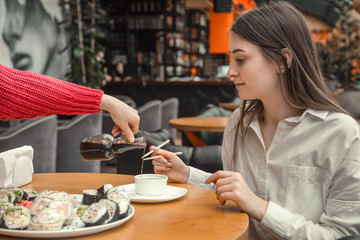 Woman pouring soy sauce on sushi roll. Sticks of sushi soy sauce