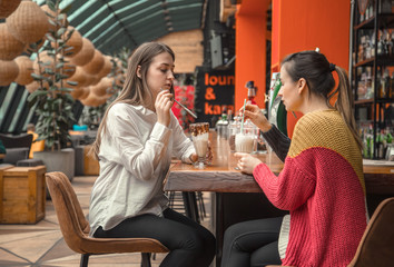 Two happy women are sitting in a cafe, drinking milkshakes,