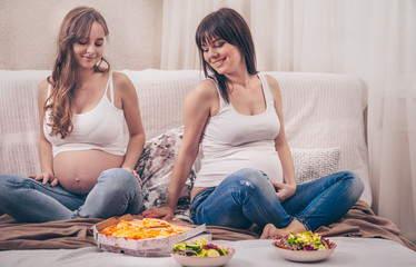 Obraz na płótnie Canvas two pregnant women eating pizza and salad at home