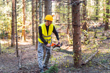 Naklejka na ściany i meble Young lumberjack working with chainsaw in forest