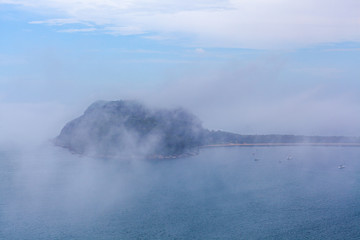 Low clouds above the ocean hiding moored sailboats and Barrenjoey lighthouse in Sydney, Australia