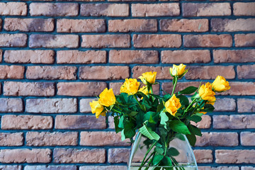 Glass vase with yellow roses  on a background of a red brick wall.