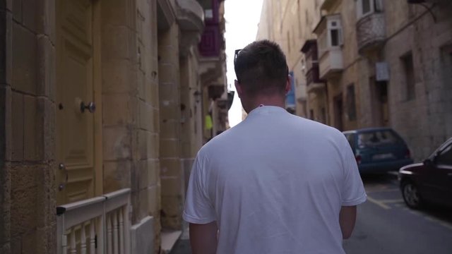 A middle plan from the back of a man walking at the typical narrow streets with colorful balconies in Valletta , Malta