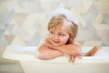 Little baby taking a bubble bath in a beautiful bathroom with a blue wall and flowers. Children's...