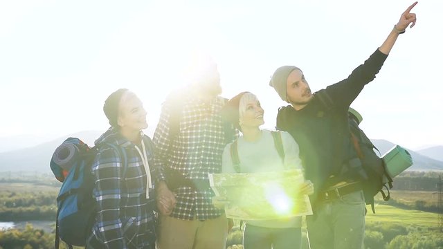 Group of caucasian travelers friends are checking the map trying to find out the right way on mountain top at sunset. Tourism and healthy lifestyle concept. Dolly shot