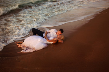happy beautiful young couple in wedding dress and suit by the sea at sunset, waves 