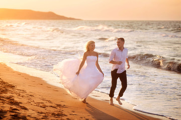 Fototapeta na wymiar happy beautiful young couple in wedding dress and suit by the sea at sunset, waves 
