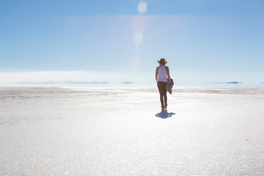 Rear view of woman walking on Bonneville Salt Flats against blue sky during sunny day