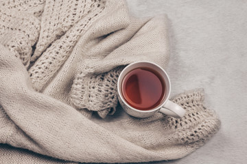 Cozy warm pastel knitted sweater along a cup of tea on milky white fur background. Get over flu concept. Top view. Copy space.
