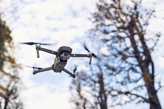 Low angle view of quadcopter flying against trees and cloudy sky