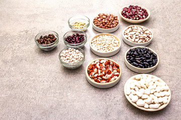 Assortment of beans on a stone background. Crimson cranberry, red, painted pony, black turtle, brown, black-eyed, Jacob's Cattle (heirloom), lima, navy, asparagus bean and soybean.