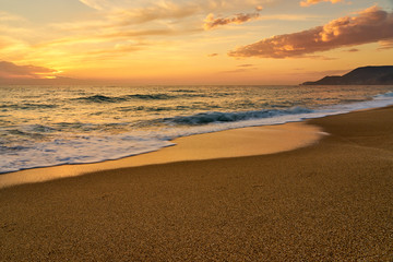 Colorful sunset at the tropical sandy beach, waves with foam hitting sand. Copy space.