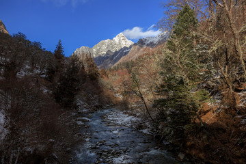 Fototapeta na wymiar Picturesque winter scenery - Snow Covered River, Four Girls Mountain National Park in Sichuan Province, China. Changping Valley, Blue Sky, white puffy clouds, Snow Covered Mountains. Siguniangshan
