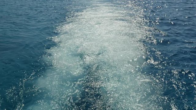 Long foamy waterway full of splashing white water trailing after a motorboat  