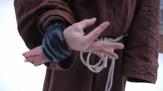 Horror hand. Man in monk outfit hold severed joke hand and wiggles fingers. Handheld shot with stabilized camera. 