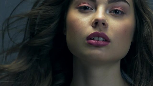 Beautiful woman with long curly hair. Attractive fashion model with a purple lipstick on the lips.  Closeup caucasian face of a girl. Slow motion footage. Sexy brunette lady.  