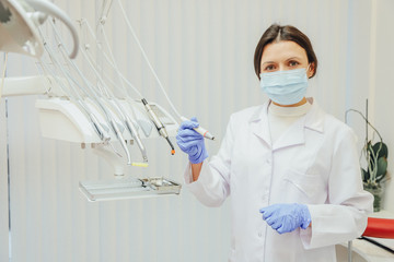 Concept of people, medicine, dentistry and healthcare - happy young woman dentist with tools above the background of a medical office.