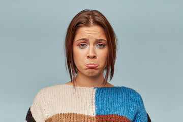 Headshot of emotional woman with a sad expression on face, crooked lower lip with a disgruntled look. The girl received bad words about her work, feels disappointed, isolated over blue background