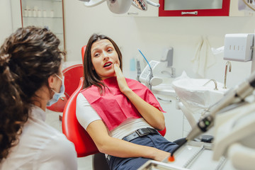 Close-up portrait of a sad young girl with a painful tooth, a doctor in office chairs, an isolated...