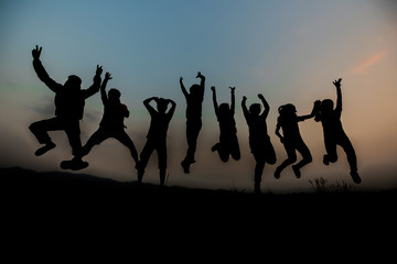 silhouettes; Group of happy people playing at summer sunset in nature