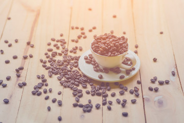 White cup full of coffee beans on Roasted Coffee Beans and wood background, top view