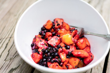 Closeup of purple red mango fruit blueberries vegan vegetarian salad on wooden picnic table with fork in bowl and orange vibrant color