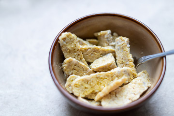 Closeup of bowl with sliced cut tempeh fermented soybeans on table cooking ingredient