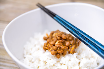 Blue chopsticks macro closeup on Asian Japanese natto fermented soy dish meal sticky slimy texture in plain white steamed rice in bowl
