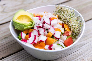 Closeup of vegan salad bowl with alfalfa sprouts, avocado half and chopped radish bell pepper mix for lunch or dinner healthy nutrition