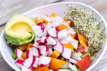 Closeup of raw vegan salad bowl with alfalfa sprouts, avocado half and chopped radish bell pepper mix for lunch or dinner healthy nutrition