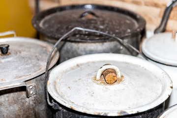 Closeup of many large pots and pans lids on rustic dacha country home or house cottage kitchen stove with dirt
