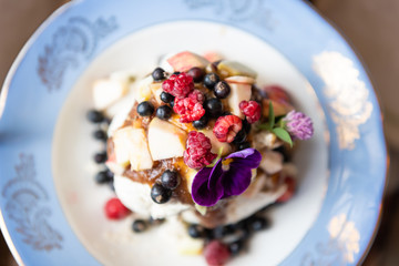 Flat top view of homemade raw vegan ice cream and fresh fruit berries from garden on plate with date syrup topping and purple pansy edible flower
